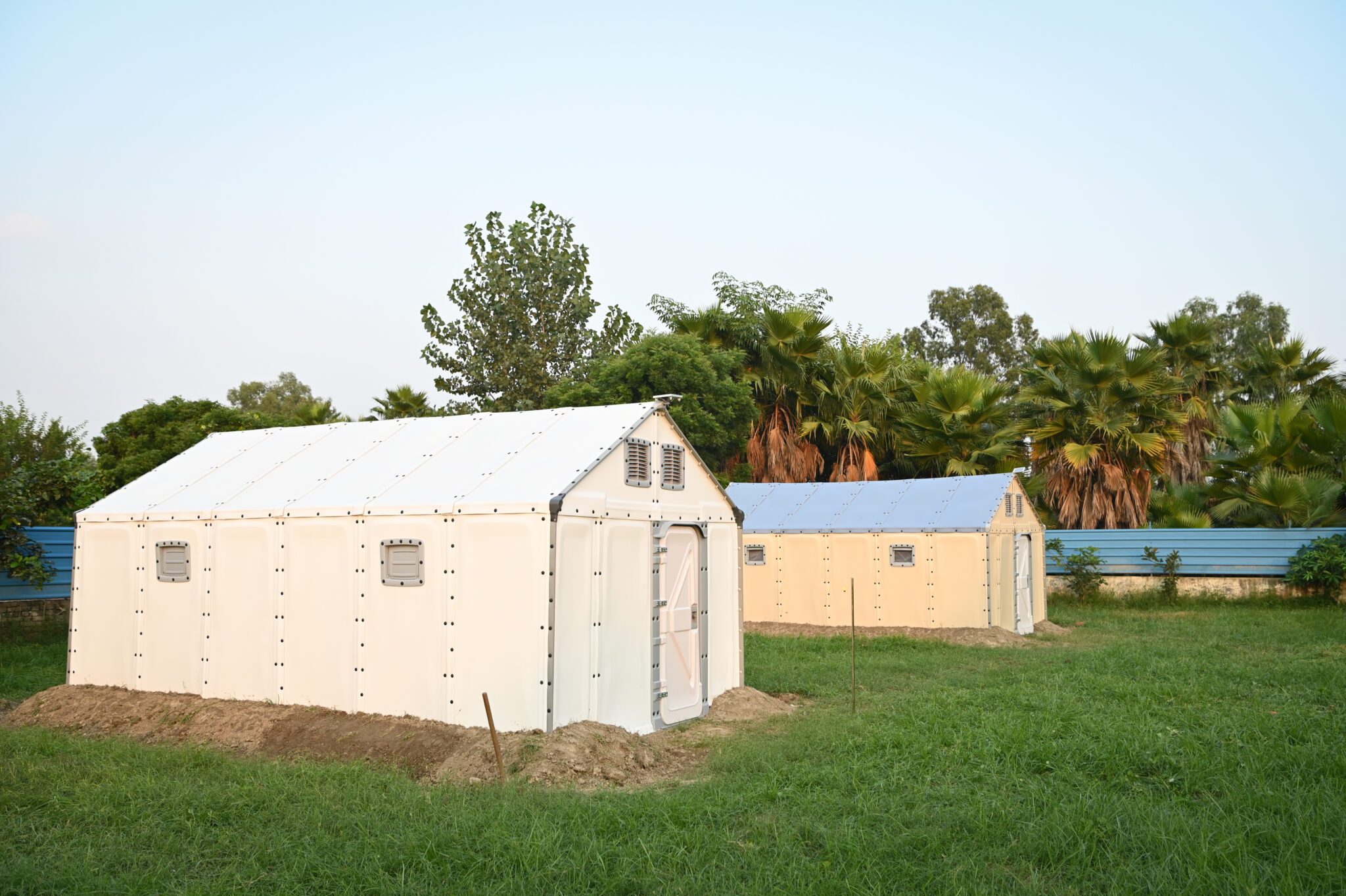 Every degree matters: testing and improving shelter temperatures with partners in India Two Better Shelter RHUs standing side by side on a grass field in Noida, India, with palm trees behind them.