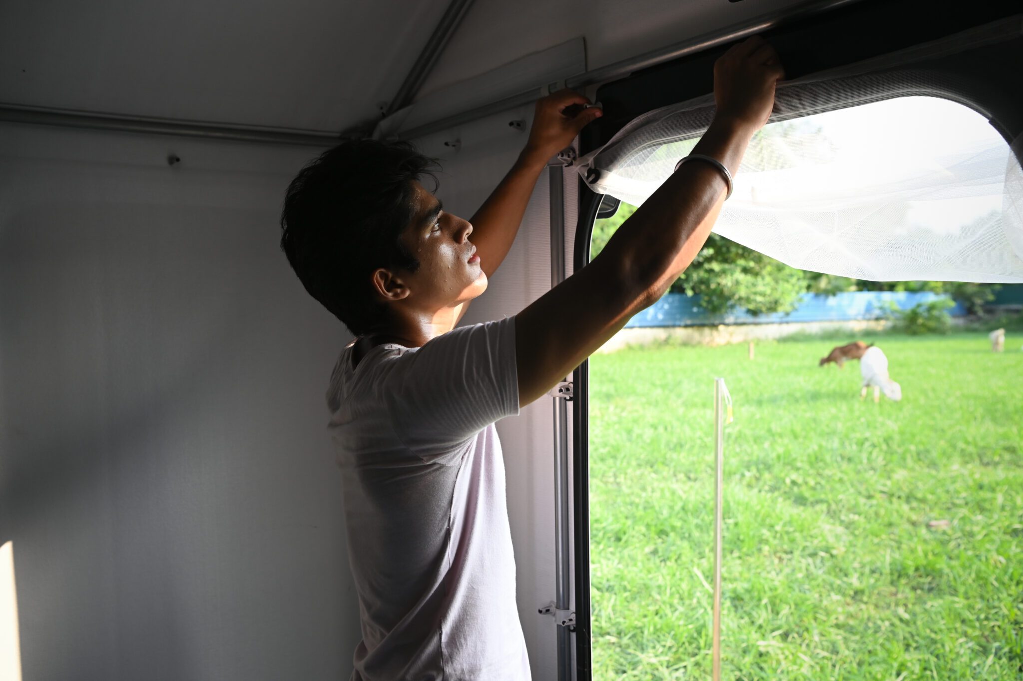 Every degree matters: testing and improving shelter temperatures with partners in India A young man fitting a net over the window opening of a shelter, with a green field outside.