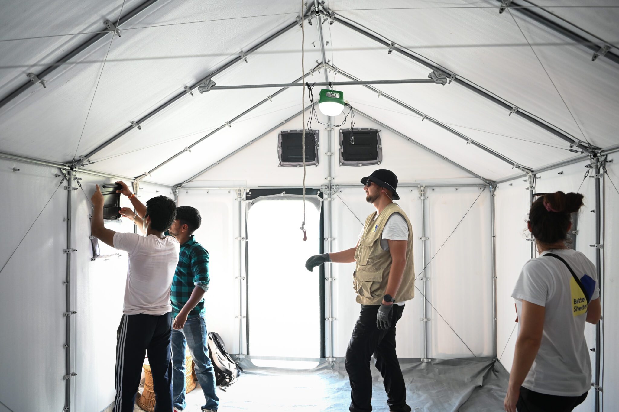Every degree matters: testing and improving shelter temperatures with partners in India Inside an RHU, two men fit a window panel while two colleagues watch. Daylight comes through the open door.